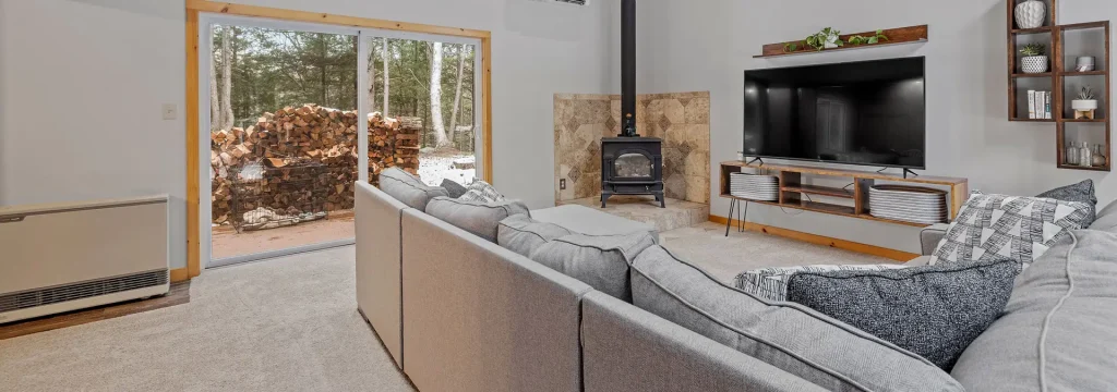 Living room setting with a fireplace and large TV. Outside a large sliding glass door is a pile of firewood and snow in the background.