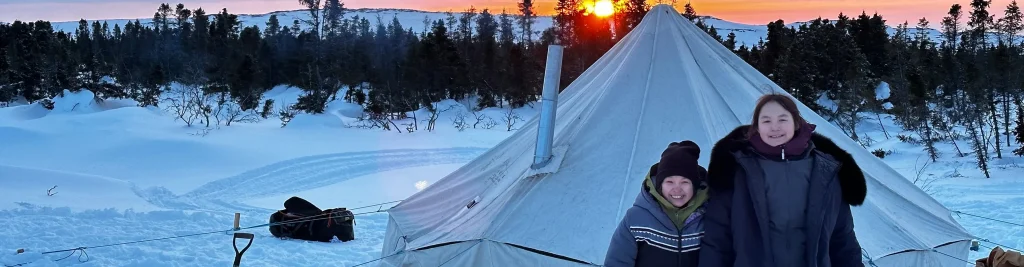 two young kids standing in-front of a winter tent with snow in the background