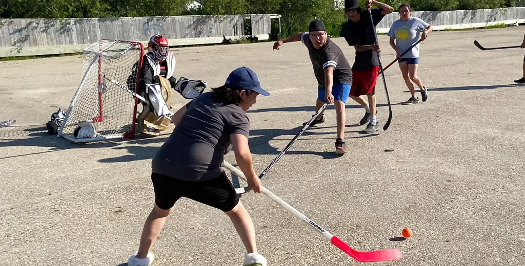 Kids playing street hockey with a orange ball and a goalie in equipment guarding the net