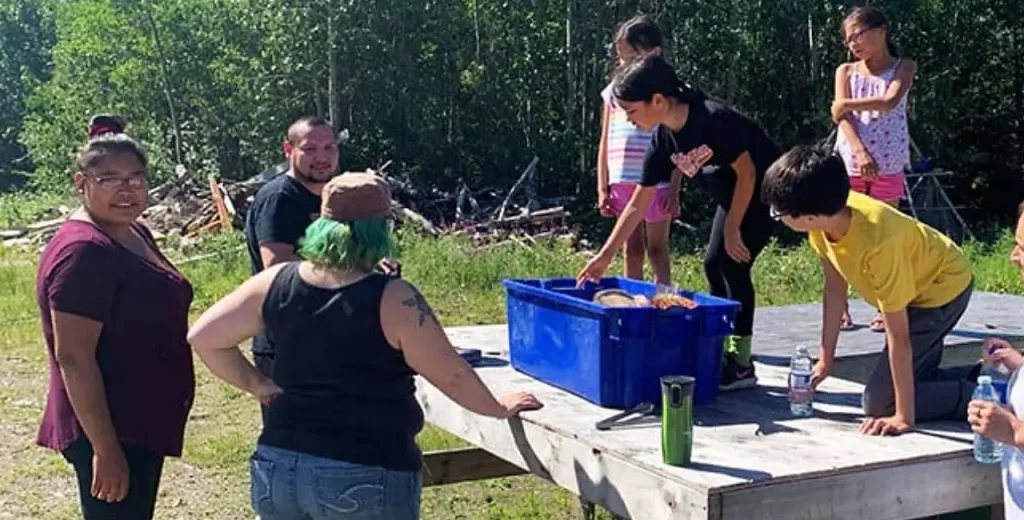a family standing around a wooden picnic table with a blue container on it