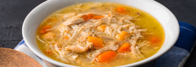 white bowl of soup with Chicken noodle soup, chicken and noodles and carrots on top.