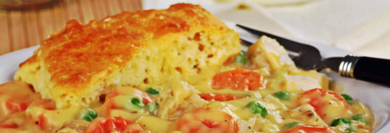 golden chicken pot pie on a white plate with a fork on the side