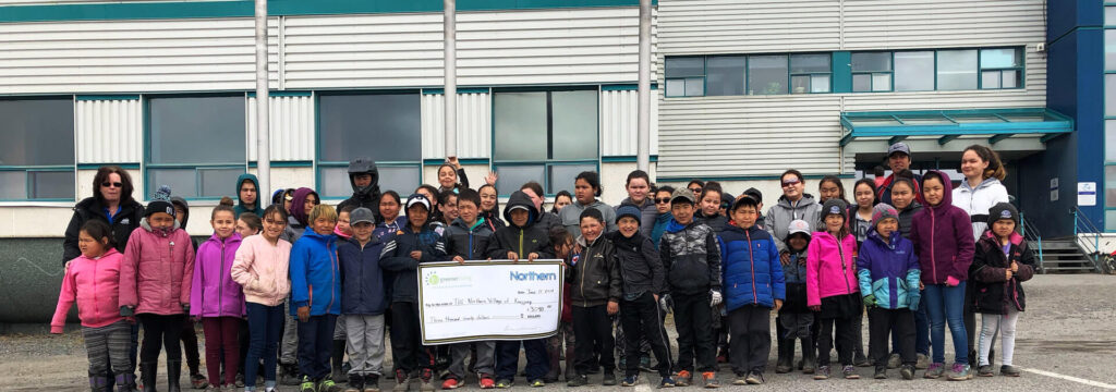 school children standing outside the school holding a large cheque
