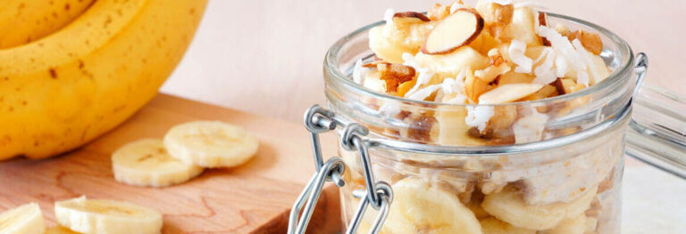 jar with oats and sliced almonds inside. sliced banada beside on a chopping block