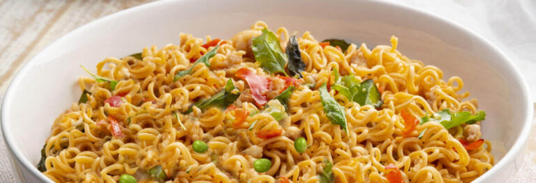 Golden noodles with peas, peppers in a white bowl