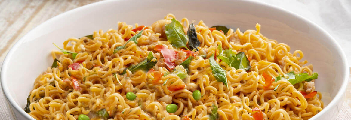 Golden noodles with peas, peppers in a white bowl