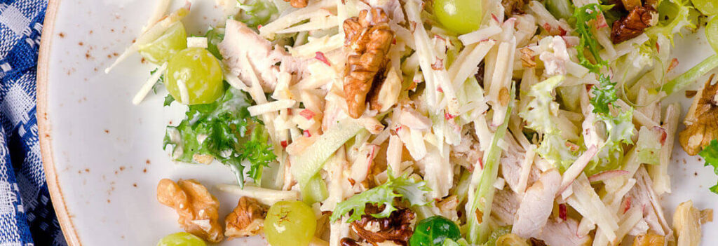 shredded chicken breast with lettuce and grapes on a white plate with a blue tablecloth under it
