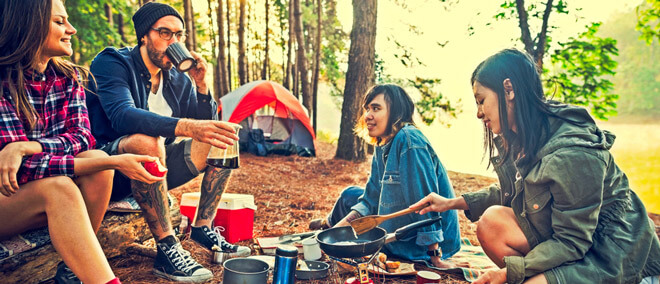 four young people sitting and cooking a meal with a tent in the background