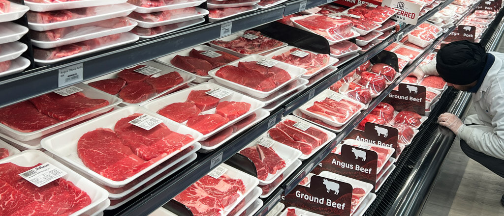 Various meats on a shelf with a worker stocking the shelf