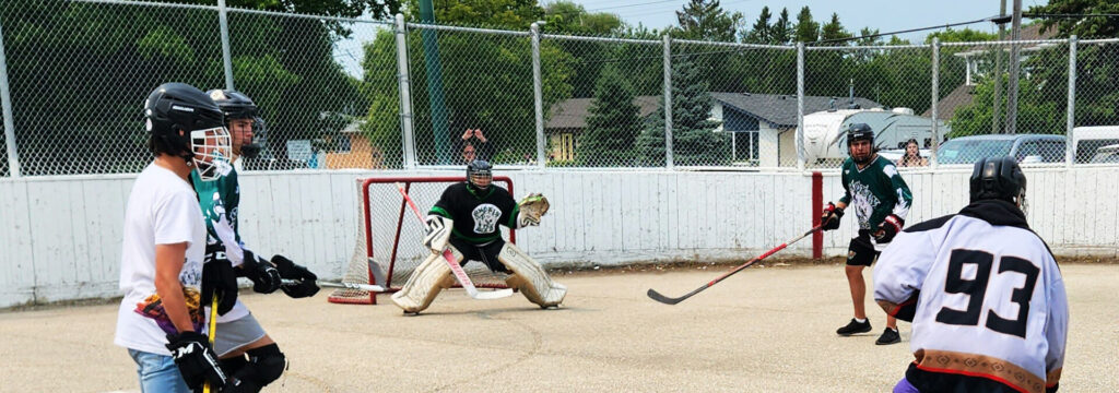 kids wearing different hockey jerseys playing ball hockey on cement in a outdoor hockey rink