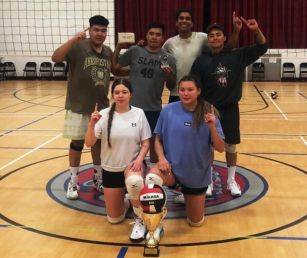 teens posing with a trophy in front of a volleyball net