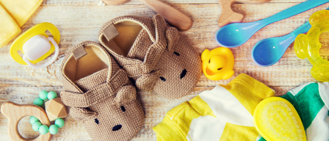 brown knitted baby booties on top of a blanket, baby toys lying around along with blue baby spoons